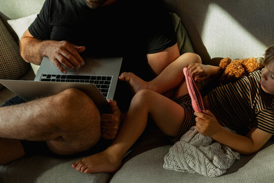 High Angle View Of Male Freelancer Working On Laptop With His Son Using Digital Tablet In Living Room