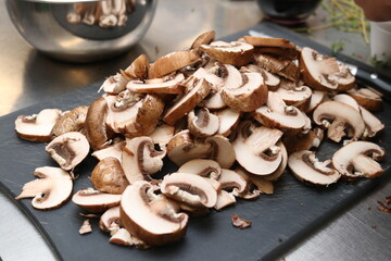 Brown capped mushrooms sliced and heaped in a stack on a black cutting board.