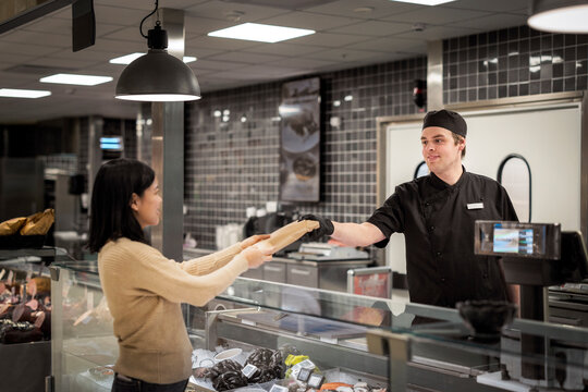Smiling young male butcher giving package to female customer