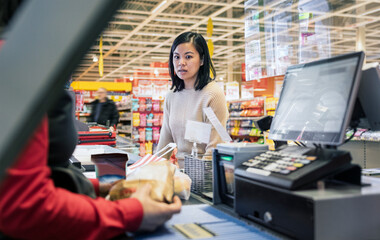 Young female customer talking to cashier at supermarket checkout