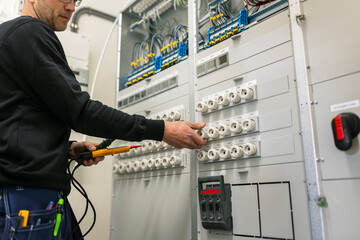 Midsection of repairman with voltage tester repairing switchboard in industry