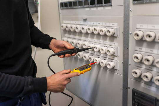 Midsection of male electrician with voltage tester repairing switchboard in meter room