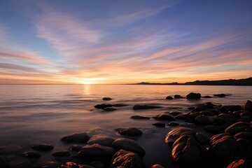 Obraz premium 夕日が沈む夕焼けのビーチの岩場の美しい風景、水と砂に夕日が反射して輝いている