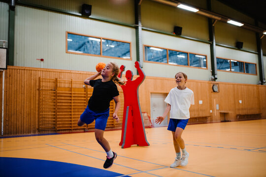 Girl jumping while playing handball with female friend in sports court