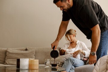 Man pouring coffee while woman breastfeeding son at home