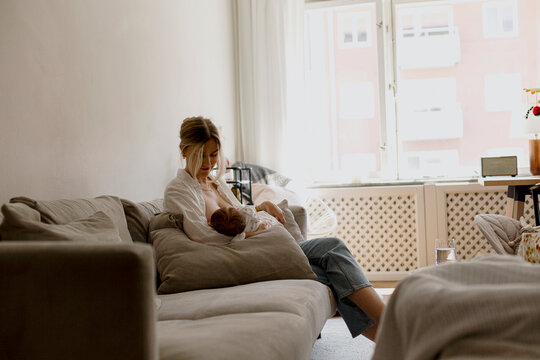 Mother breastfeeding son while sitting on sofa in living room at home