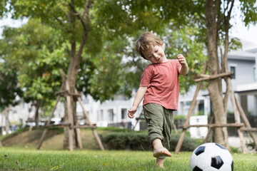 Cheerful little boy playing soccer in the park. Little boy playing football in the garden