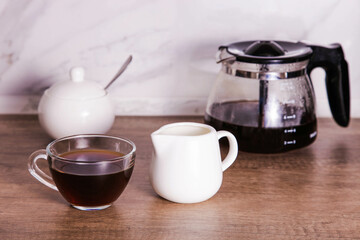 Coffee in glass cup with milk jug on the table