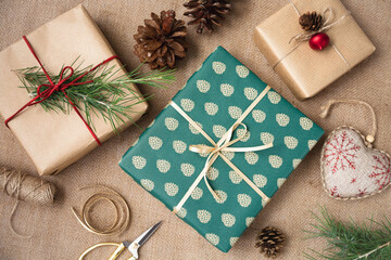 Gifts packed in paper, rope, spruce cones and scissors are on the table. Preparation for Christmas. View from the top.