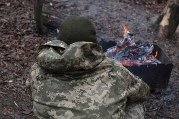 A Ukrainian soldier is warming himself by a fire in the forest