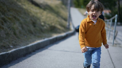 Close-up of elated boy in yellow pullover sprinting in autumn?Cheerful child's face captured...