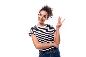 young smiling curly brunette lady with black hair is dressed in a striped t-shirt showing three fingers