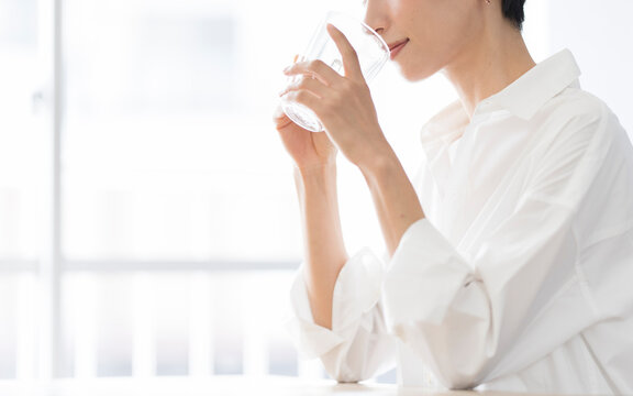 グラスに入った飲み物を飲む女性/白いシャツを着たミドル世代の日本人女性
