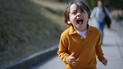 Close-up of elated boy in yellow pullover sprinting in autumn?Cheerful child's face captured mid-run on a fall day