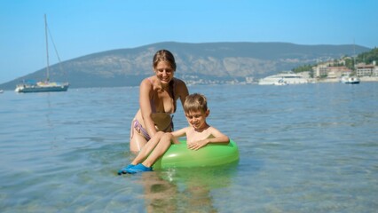 Happy smiling mother with son swimming in inflatable swimming ring at the sea beach. Family holiday, vacation and fun summertime of children and parents.
