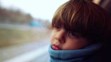 Introspective young boy with scarf, nestled by the train window, lost in contemplation as the...