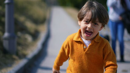 Joyful excited little boy running outside during autumn day wearing yellow pullover. Close-up face...