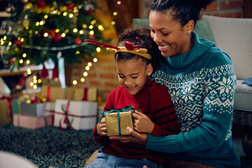 Happy black girl receives Christmas present from her mother at home.