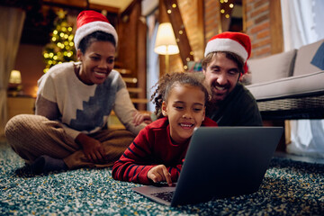 Black little girl using laptop with her parents at Christmas Eve.