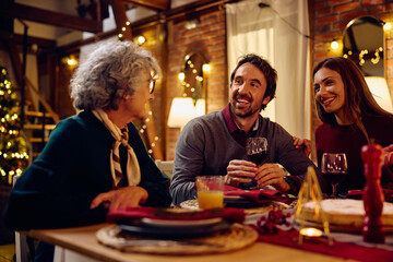 Happy couple talking to their senior mother at dining table on Christmas Eve.