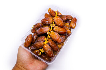 Close-up view of Transparent food container filled with large delicious Sukkari dates pile to keep food hygienic isolated on white background. Arabic healthy food concept.