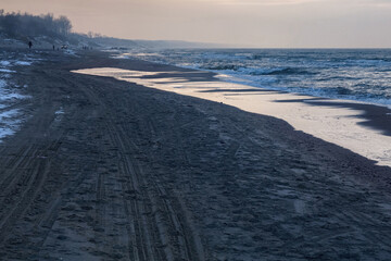 View of the sand beach with the tire marks and footprints on the Baltic Sea coast on the Vistula Spit at the winter time.