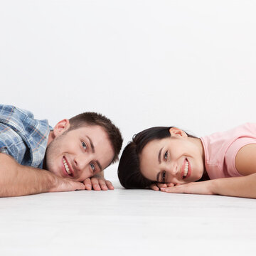 Front view of happy young couple looking at the camera and smiling while lying on wooden floor. Woman and man holding hands and very happy