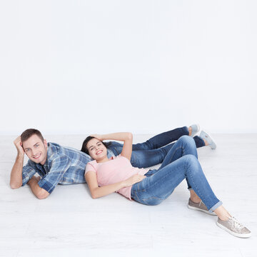 Happy young couple, lying on the floor, look at each other and dream of furniture for a new apartment.