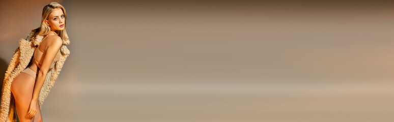 Fototapeta premium attractive blonde woman in beige sexy lingerie and faux fur bending her body slightly, banner