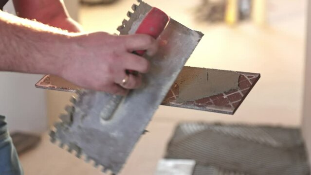 Professional tiler applying adhesive glue to tile for tiling the floor, industry building concept
