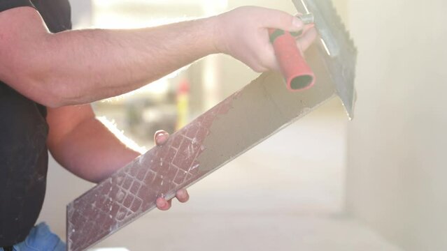 Professional tiler applying adhesive glue to tile for tiling the floor, industry building concept