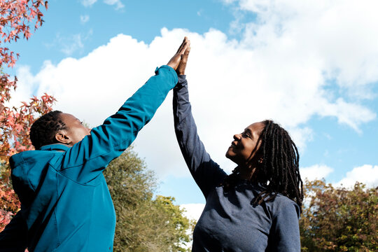 Two black mature fitness women making high five outdoors.