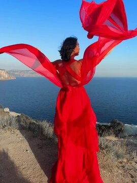 woman sea red dress. A beautiful sensual woman in a flowing red dress and with long hair, standing on a rock above the beautiful sea in a large bay.