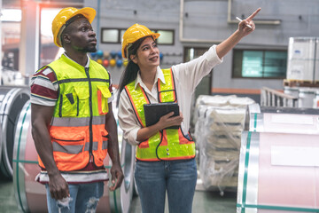 team of female engineers and black male laborers wearing uniforms and hard hats walk together to inspect roof quality and maintain machinery in a factory and warehouse.