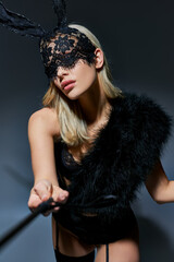 portrait of blonde hot woman in lace underwear and rabbit mask pointing bdsm whip at camera
