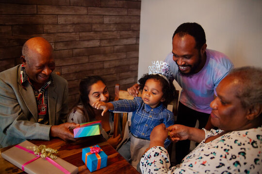 Multiracial parents and grandparents celebrating baby's birthday with presents and tiara at home