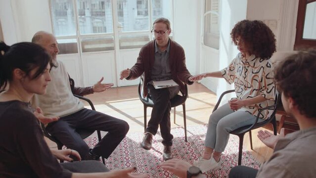 Therapist and patients sitting in a circle, holding hands and closing their eyes during group therapy session. Zoom shot