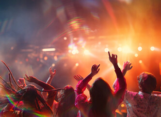 large group of people having fun, singing and dancing raising hands on concert of favorite artists in neon light, spotlights near stage