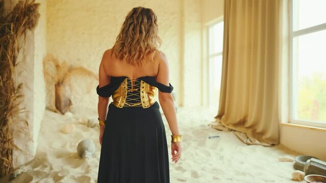 fantasy sexy woman walking in room full sand desert. blonde hair beauty princess. fashion model girl go to panoramic window back rear view waiting love. black gold long dress old style art video 4k