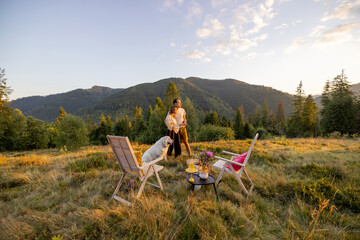 Man and woman have a picnic while spending summer time together in the mountains. View on beautiful meadow on sunset