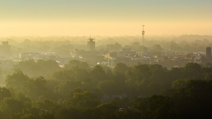 Hazy yellow sunrise with smog over city and green summer trees in Muncie, Indiana