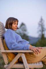 Fototapeta premium Portrait of a thoughtful woman sitting on wooden chair while resting in the mountains