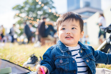 秋の木漏れ日の中、芝生の上でピクニックランチを楽しむ1歳の笑顔の赤ちゃん