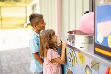 Little girl and boy waiting for a sweet cotton candy to be made at the counter shop while visiting...