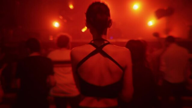 Girl dancing at nightclub party in red light, back view. People jumping at rave in underground techno club. Nightlife, modern music event and entertainment concept. Slow motion