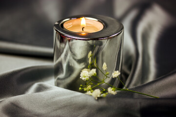 Spa still life with white small fresh blooming flowers, metallic burning candle on silk silver gray...