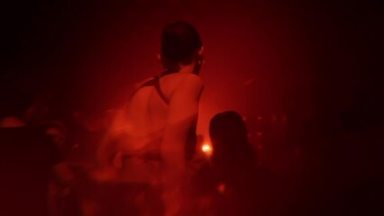 Girl dancing at rave party in techno club in crowd at electronic music festival. Young woman enjoying nightlife on nightclub dance floor with flashing red lights