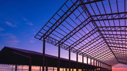 Silhouette of metal industrial buildings outline structure in construction site area against colorful sunset sky background, low angle and perspective side view 