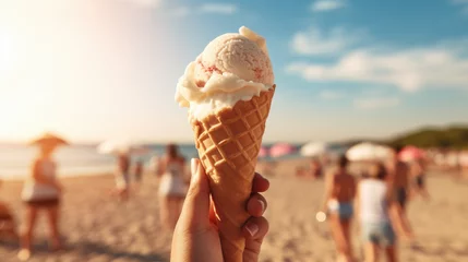 Foto auf Alu-Dibond A person holds a vanilla gelato cone on a sunny beach with friends and family in the background, capturing a perfect summer day. © Bela