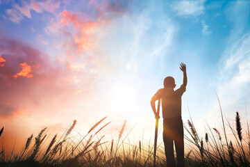 a disabled man standing up and raising his hand at sunset background